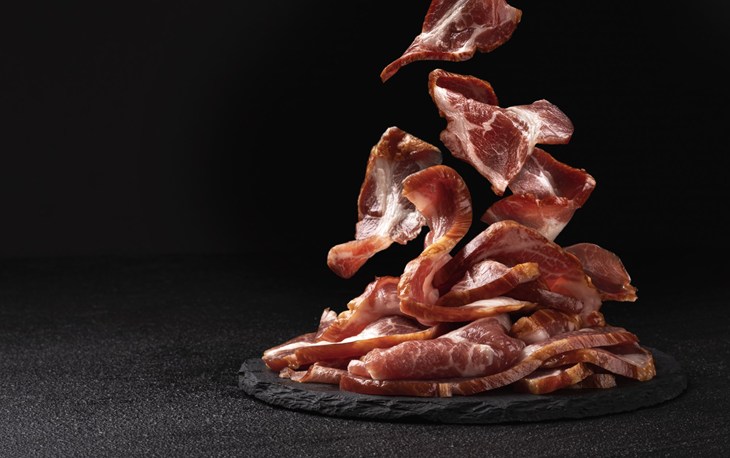lonchas de carne cayendo sobre un plato plano de color negro sobre un fondo negro