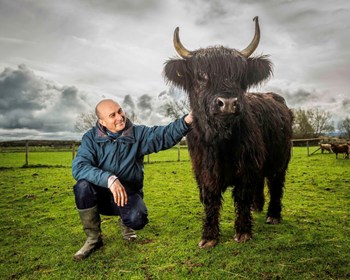 Philip con una hermosa vaca de las tierras altas de largo pelo negro en un prado